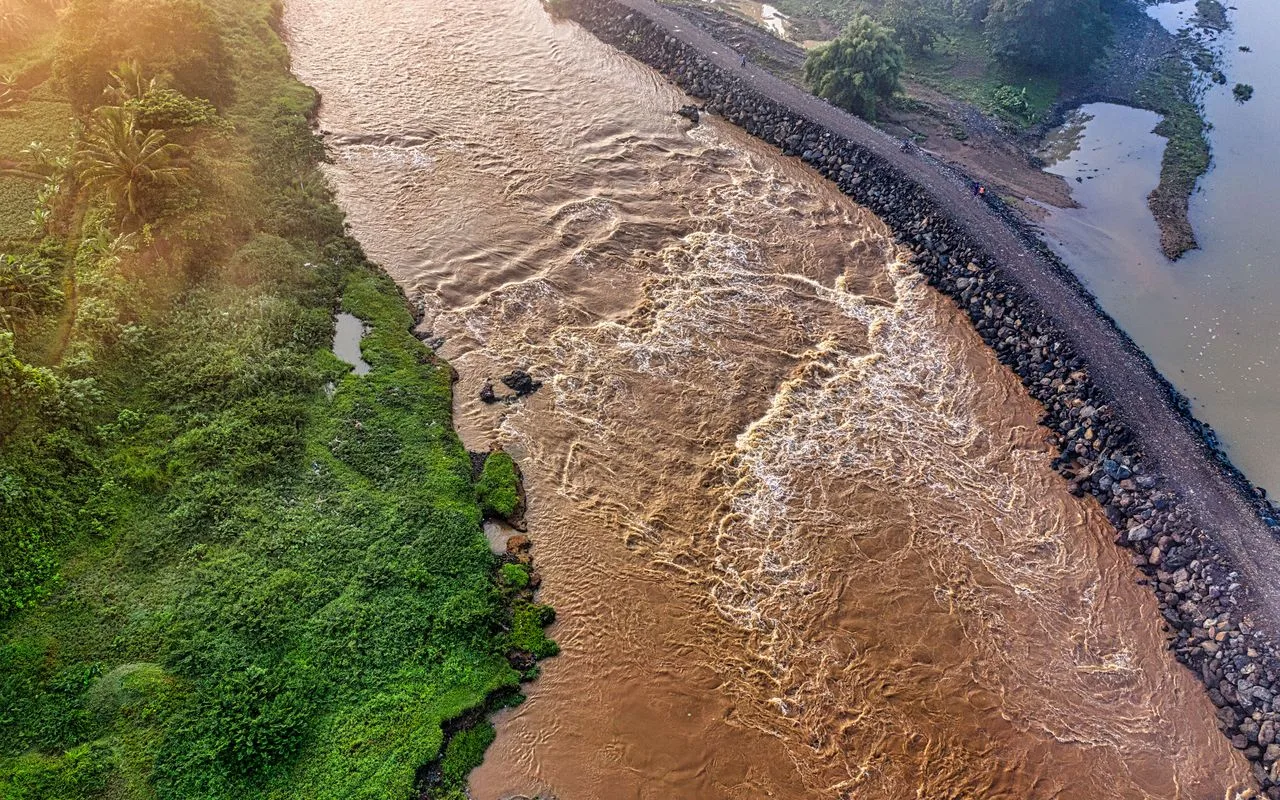 A river in flood seen from the air, the torrent held against a rock levee