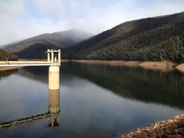 A reservoir intake tower and its footbridge beneath forested ridges