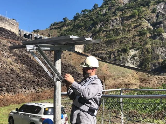An engineer fitting a solar panel to a monitoring post at a dam site